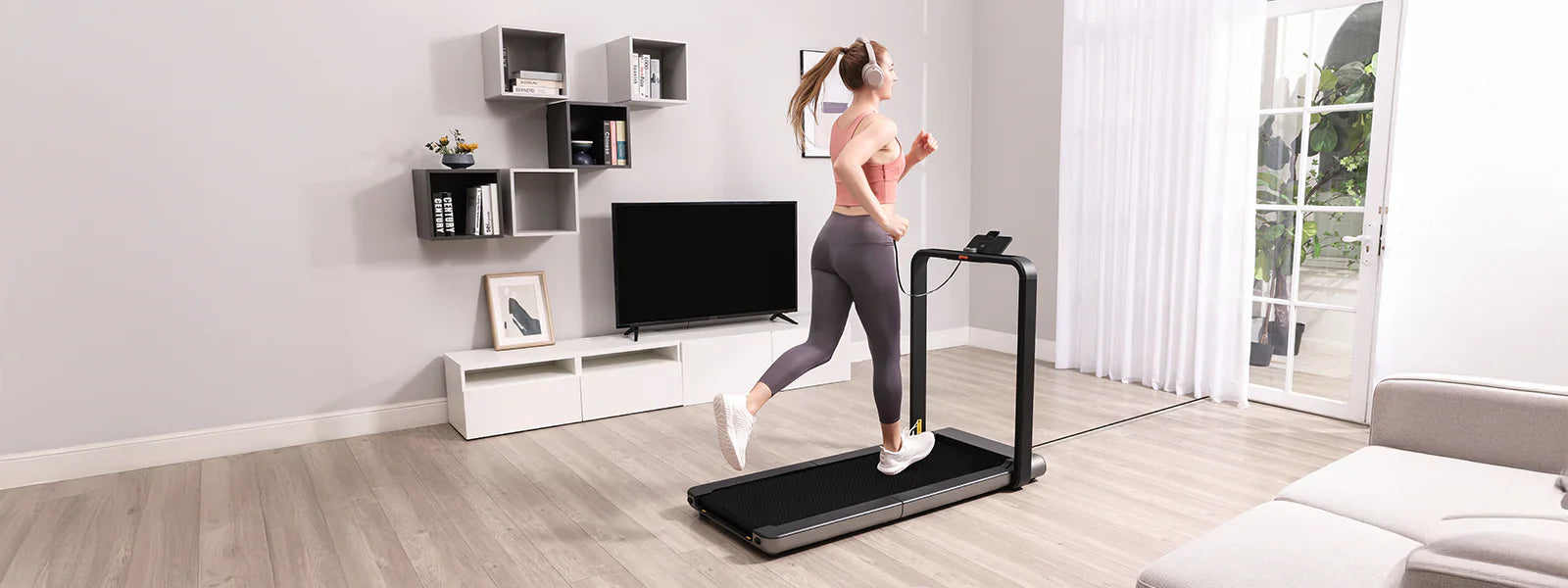 Eine Frau mit Kopfhörern läuft auf einem Laufband in einem modernen Wohnzimmer mit einem Fernseher, Regalen und einem großen Fenster.