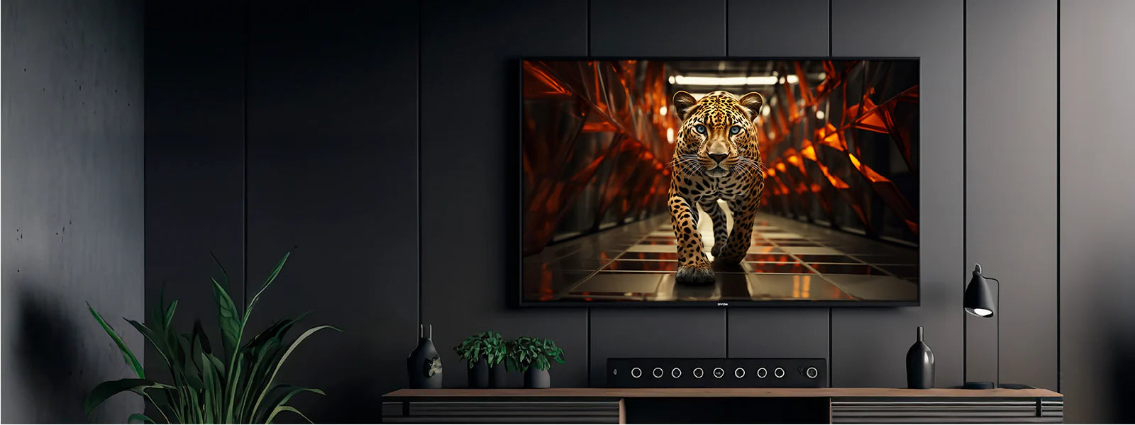 Ein an einer dunklen Wand montierter Flachbildfernseher zeigt einen Leoparden, der auf die Kamera zugeht; darunter stehen Pflanzen und eine Soundbar auf einer Holzkonsole.