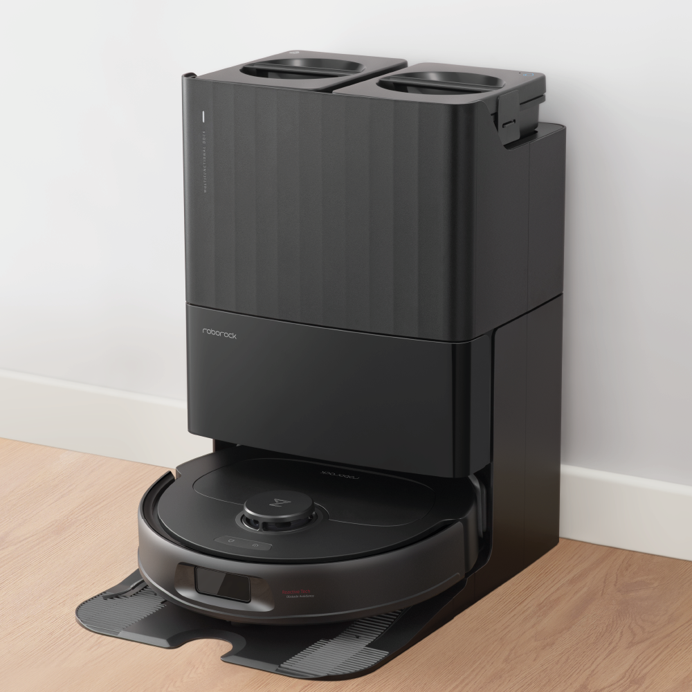 Der Roborock Qrevo Plus Black Staubsaugerroboter ist in seiner Lade- und Reinigungsstation auf einem Hartholzboden an einer weißen Wand angedockt.