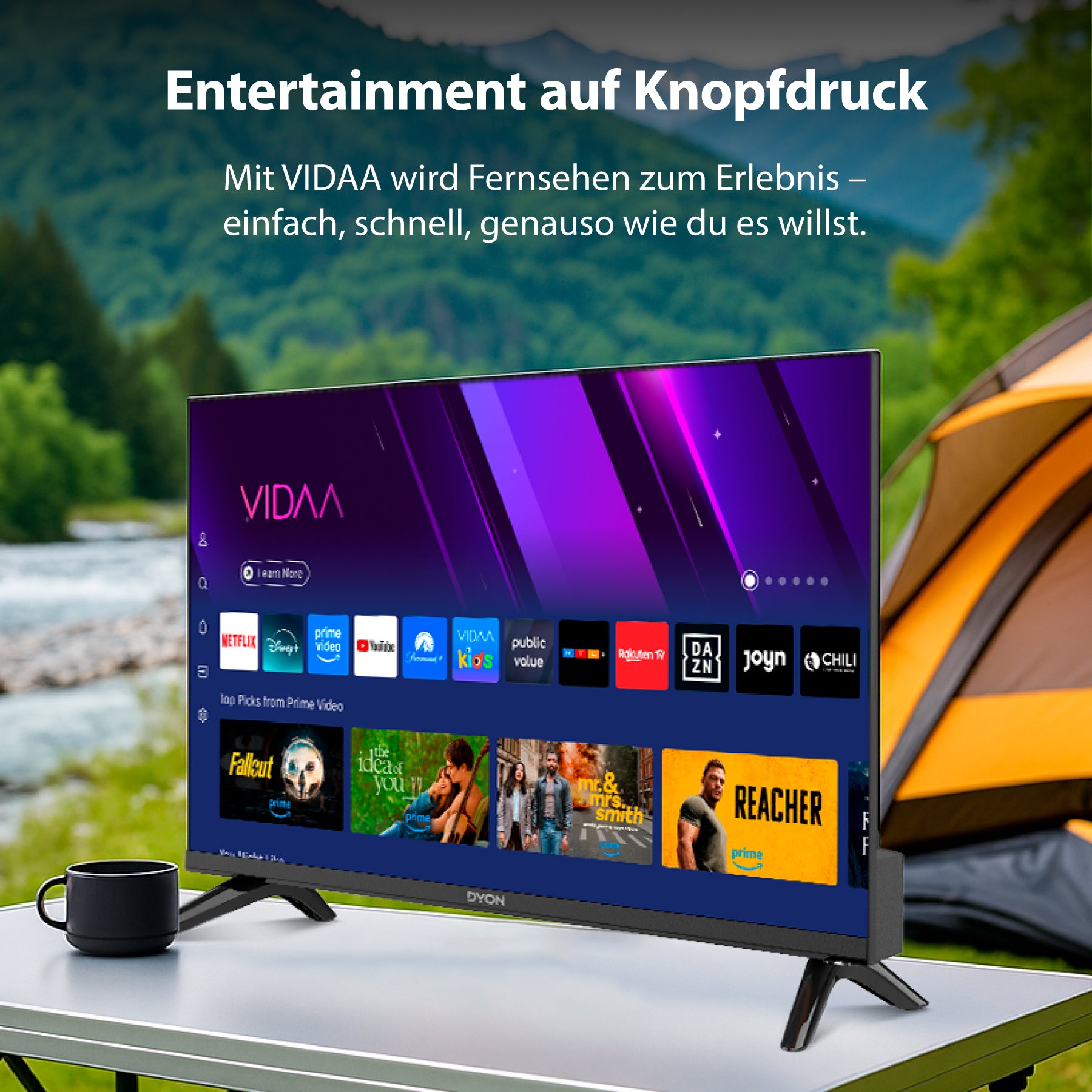 Der Dyon Smart 24 VX-V Smart TV (24 Zoll, 60 cm) steht auf einem Tisch im Freien neben einem Becher, mit einem Zelt und Grünzeug im Hintergrund und einer intelligenten Schnittstelle auf dem Bildschirm.
