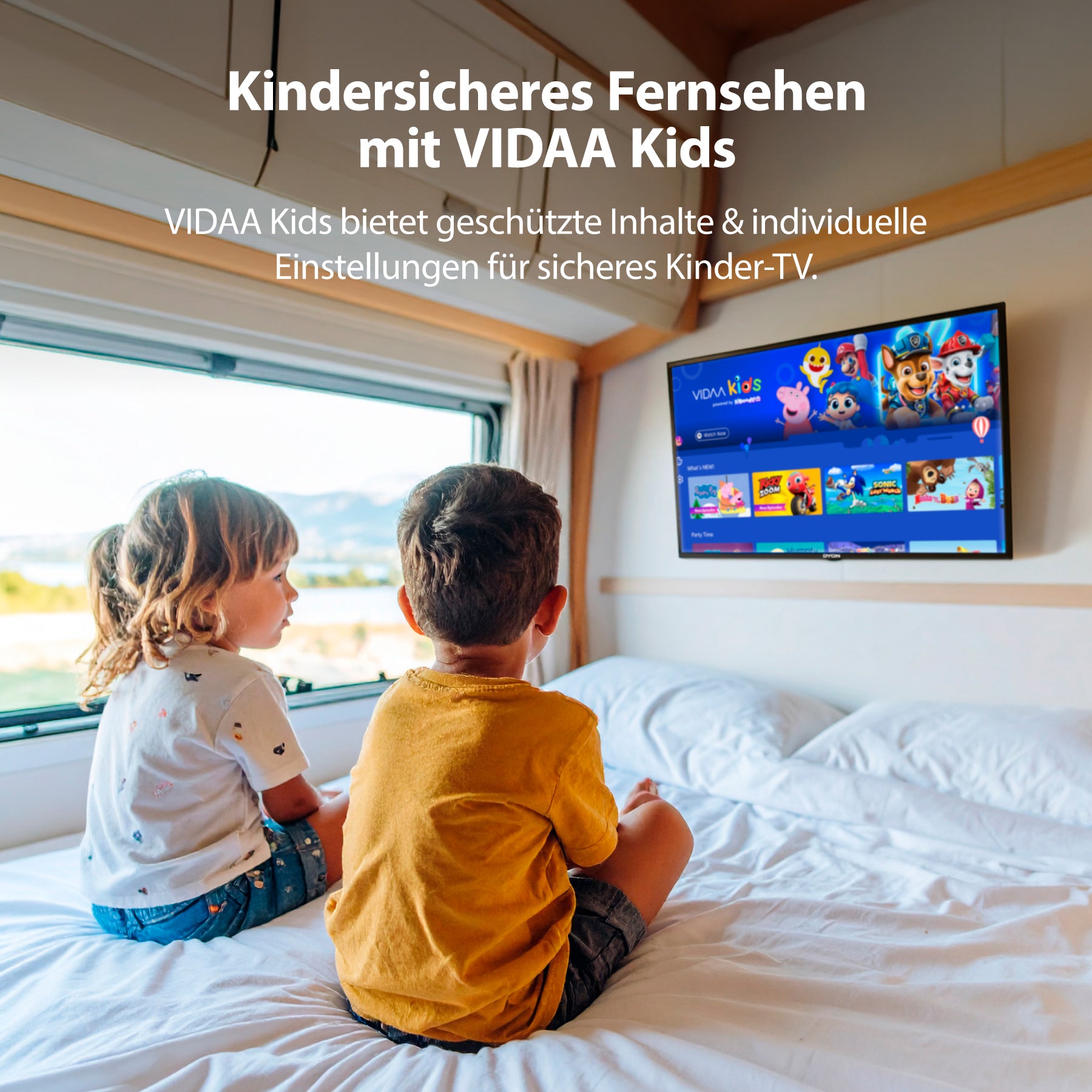Zwei kleine Kinder sitzen auf einem Bett in einem sonnenbeschienenen Raum und schauen auf den an der Wand montierten Dyon Smart 24 VX-V Smart TV (24 Zoll, 60 cm), der den Streaming-Dienst VIDAA Kids anzeigt.