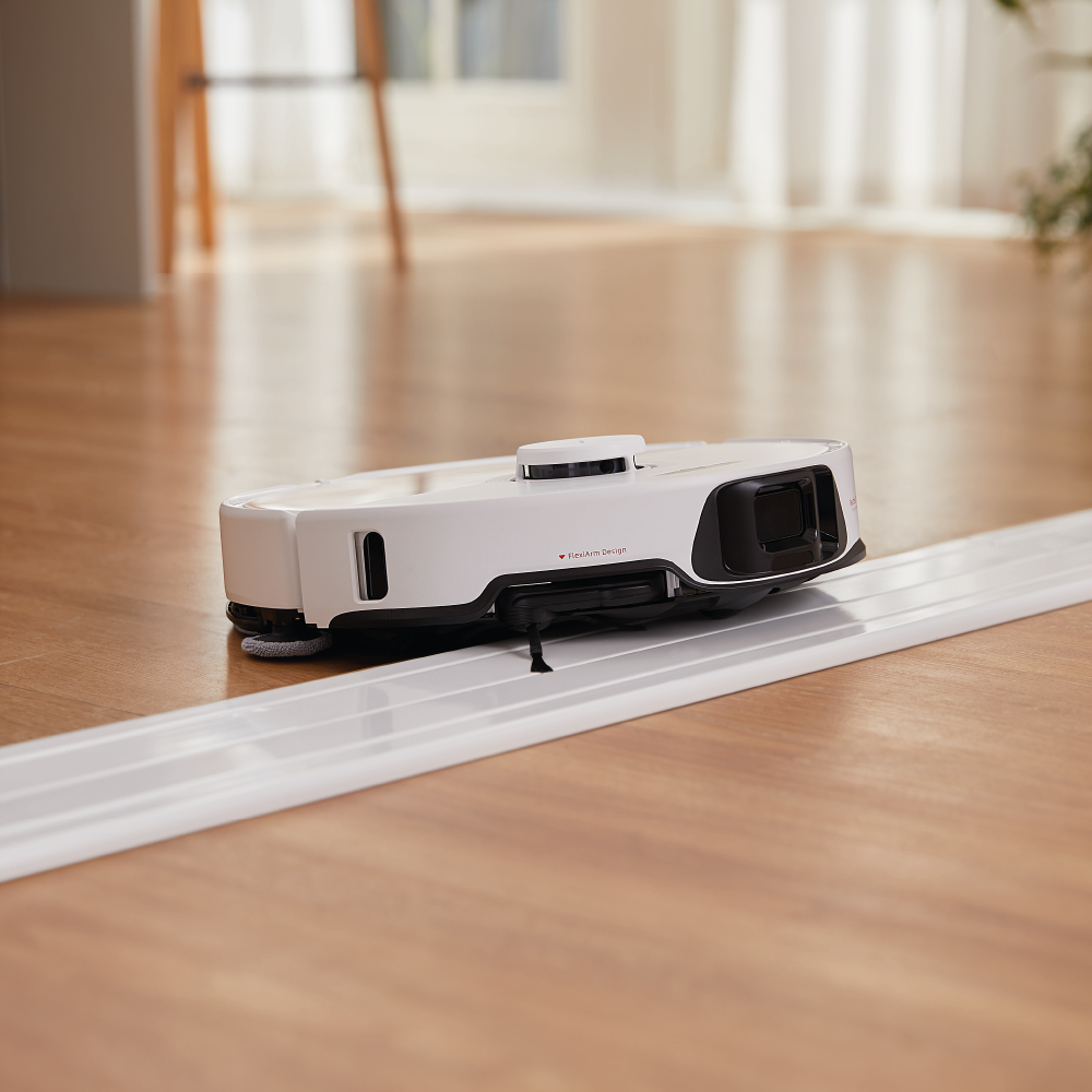 Der Roborock S8 MaxV Ultra White mit Wasseranschluss reinigt einen Holzboden an einer weißen Kunststoffschiene in einem sonnenbeschienenen Raum.