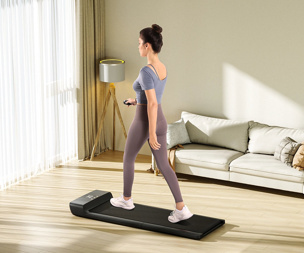 Eine Frau läuft auf einem schwarzen Laufband in einem hellen Wohnzimmer mit Holzboden, einem beigen Sofa und einer modernen Stehlampe.