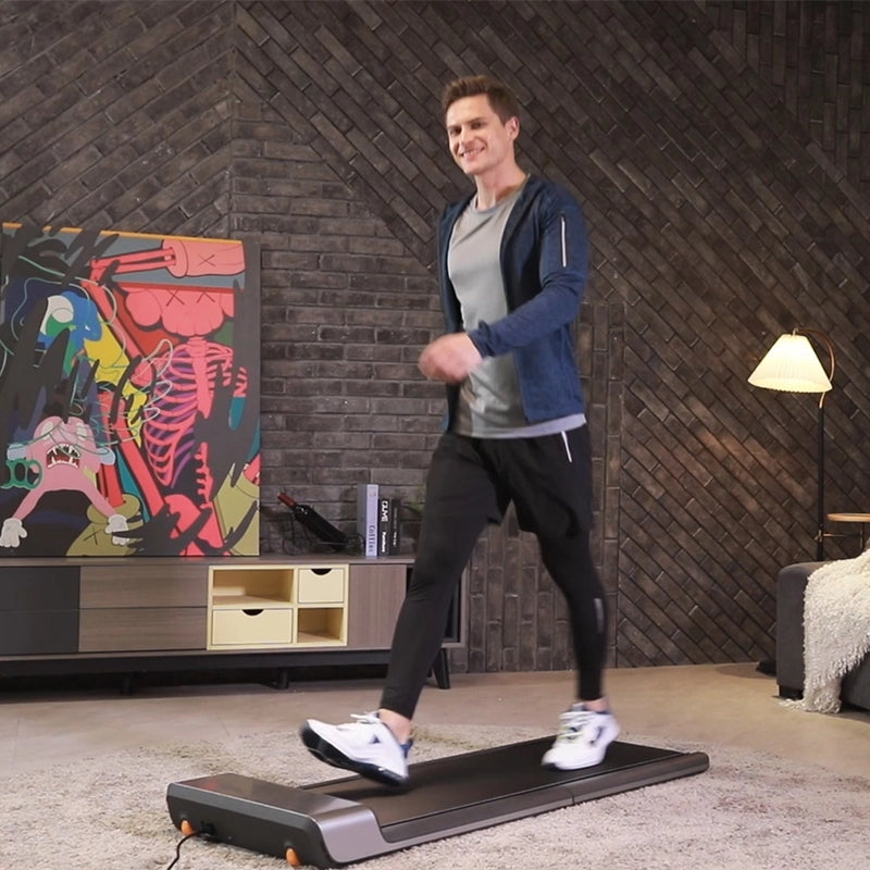 Ein Mann läuft auf einem Kingsmith WalkingPad P1 Klappbares Laufband für Schreibtisch in einem modernen Wohnzimmer mit einem bunten abstrakten Gemälde, einer Lampe und einem Sofa im Hintergrund.