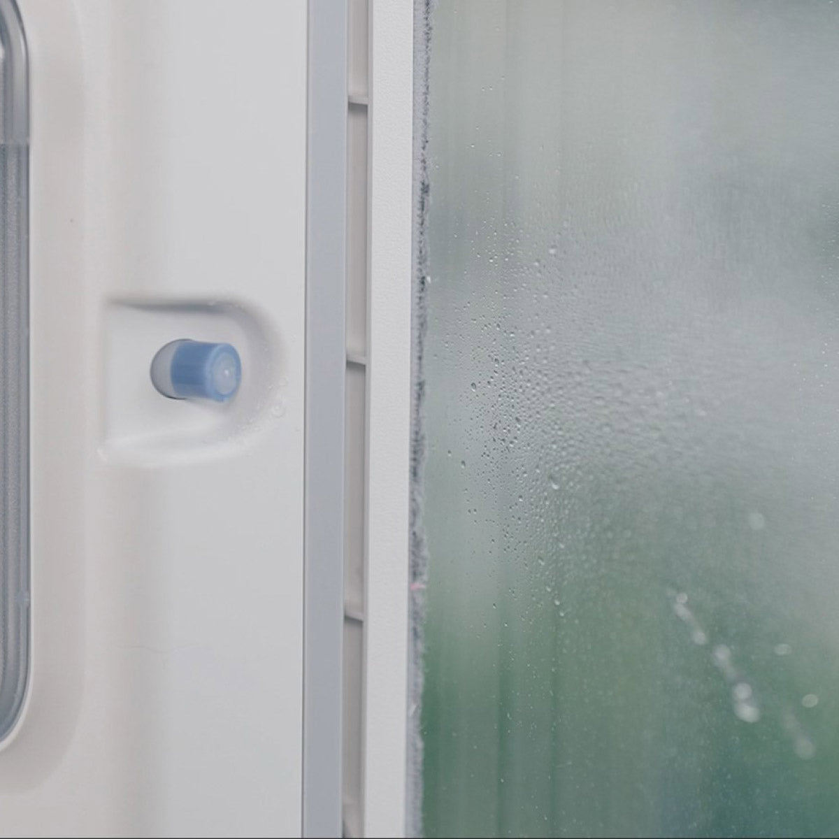 Eine Nahaufnahme eines beschlagenen weißen Fensters, Rahmens und Griffs - ideal für die Präsentation von intelligentem Fensterputzen mit dem HUTT W8 Fensterputzroboter und seinem dualen Sprühsystem.