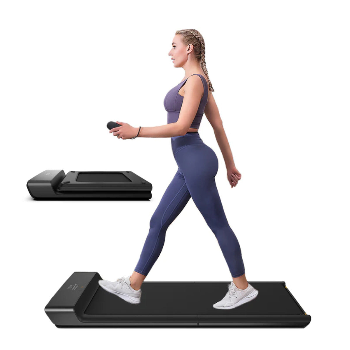 Eine Frau in Sportkleidung benutzt den Kingsmith WalkingPad A1 Pro Klappbares Laufband Schreibtisch (bis 136 kg) mit einer Fernbedienung, während ein anderes gefaltetes Laufband ordentlich im Hintergrund aufbewahrt wird.