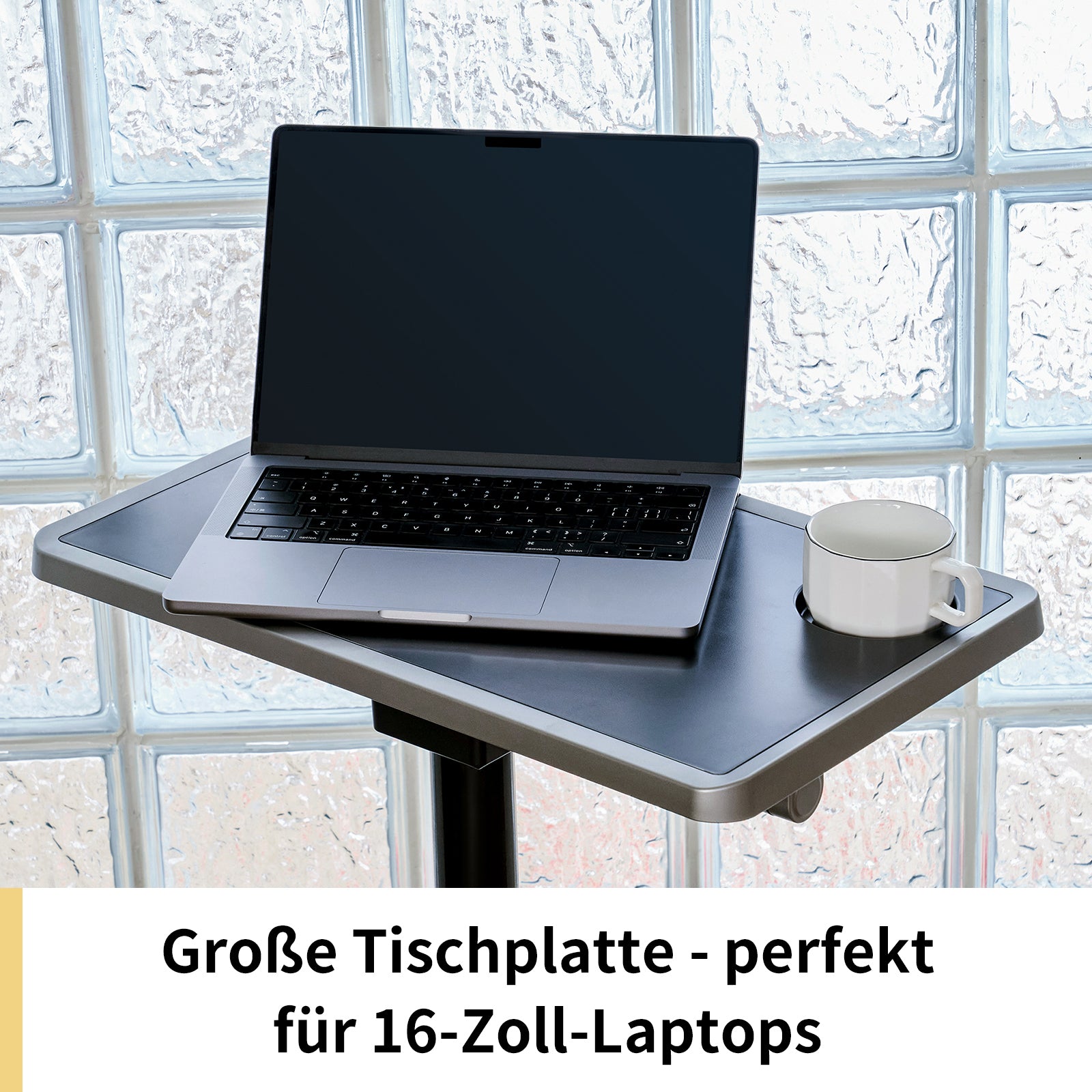 Ein 16-Zoll-Laptop und eine weiße Kaffeetasse ruhen auf einer geräumigen Tischplatte vor Glasbausteinfenstern; laut deutschem Text ist sie ideal für 16-Zoll-Laptops oder für kompakte Fitnessgeräte wie das Kingsmith Office Bike W1B von Kingsmith.