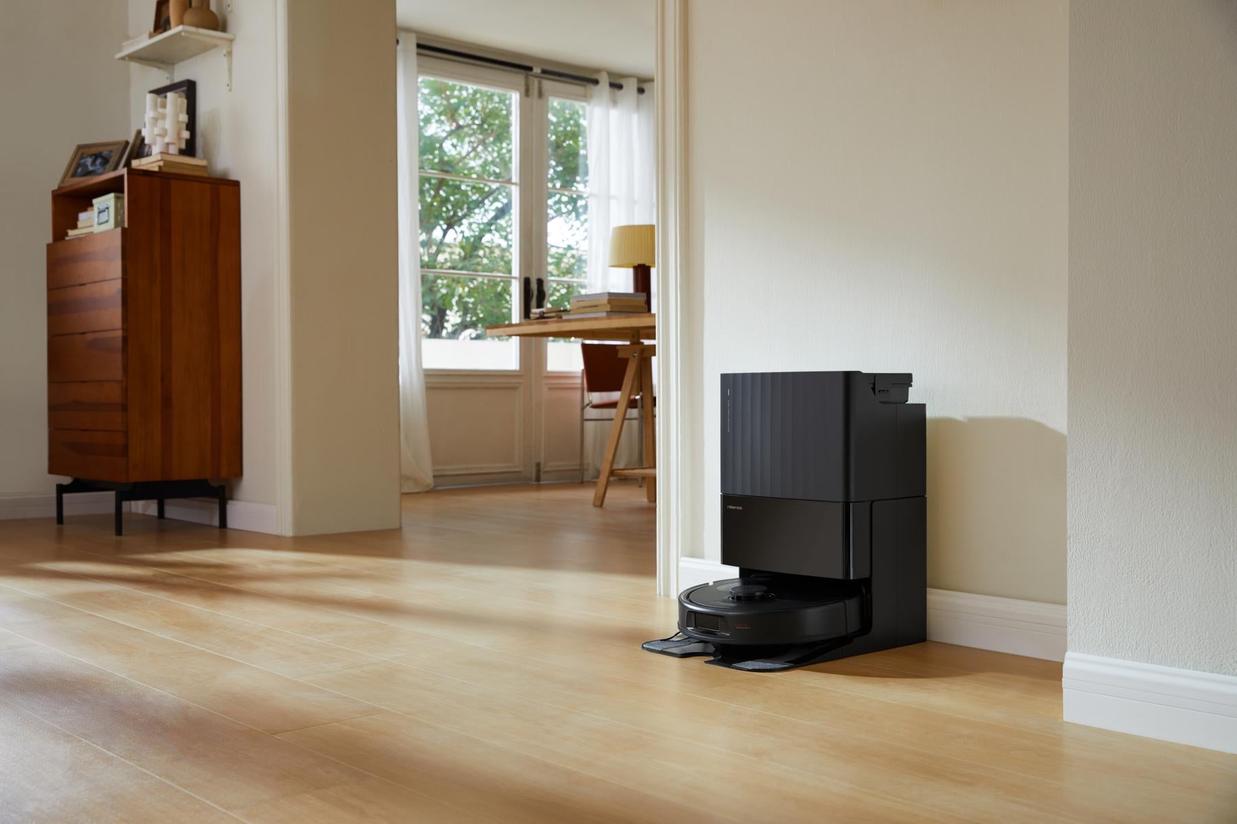 Der Roborock Qrevo 598 Black Staubsaugerroboter mit Multifunktions-Dockingstation steht vor einer weißen Wand in einem hellen, modernen Wohnbereich mit Holzböden.