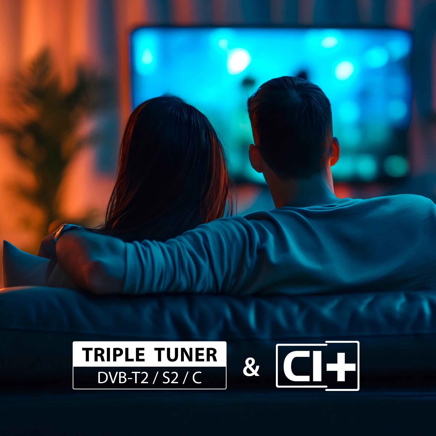 Ein Paar sitzt auf einem Sofa und sieht in einem schwach beleuchteten Raum fern. Der Text lautet: Triple Tuner DVB-T2/S2/C & CI+ auf dem Dyon Smart 50 VX Smart TV (50 Zoll, 126 cm).