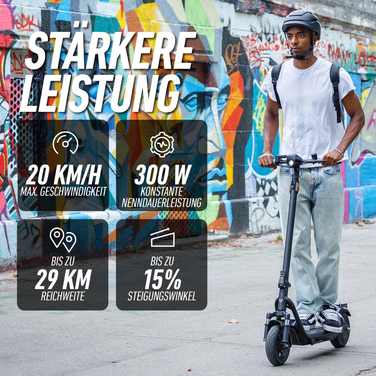 Ein behelmter Mann fährt mit dem NIU KQi100P Anthrazit E-Scooter durch die von Graffiti geprägten Straßen der Stadt - ideal für die urbane Mobilität. Technische Daten: 20 km/h Höchstgeschwindigkeit, 300-W-Motor, 29 km Reichweite, regenerative Bremse und bewältigt Steigungen von 15 %.