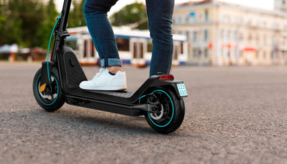 Ein Fahrer in blauen Jeans und weißen Turnschuhen gleitet auf einem Odys ALPHA X5 PRO - E-Scooter mühelos durch die Stadt, vorbei an verschwommenen Gebäuden und genießt eine Reichweite von 50 km für eine reibungslose Stadtfahrt.