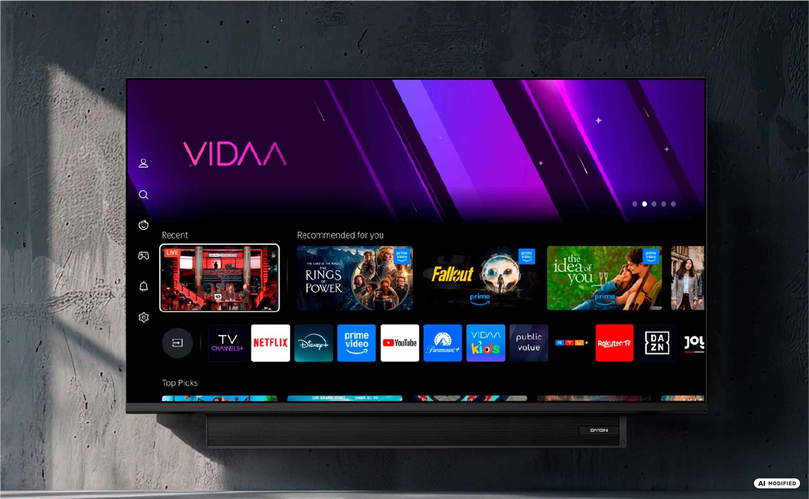 Ein DYON Movie Smart 32 VX-S 32-Zoll-HD-Smart-TV – Soundboost von Dyon ist an einer grauen Wand montiert und zeigt die VIDAA-Smart-TV-Benutzeroberfläche mit verschiedenen Streaming-Apps und empfohlenen Inhalten an.