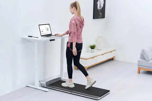 Eine Person läuft auf einem Laufband unter einem Stehpult, während sie einen Laptop in einem minimalistischen, modernen Raum benutzt.