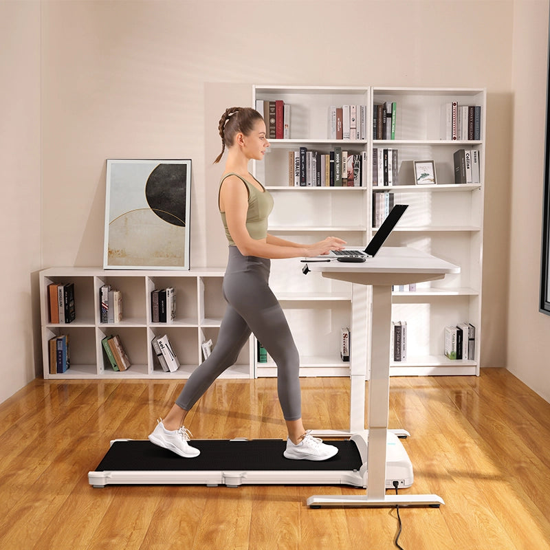 Eine Frau benutzt das Kingsmith WalkingPad C1 Klappbares Laufband, während sie an ihrem Laptop an einem Stehpult in ihrem Heimbüro mit Bücherregalen arbeitet - ideal für Homeoffice Fitness.