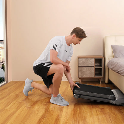 Eine Person in Sportkleidung kniet und faltet das Kingsmith WalkingPad C1 Klappbares Laufband neben einem Bett in einem minimalistischen Schlafzimmer, ideal für Homeoffice Fitness.