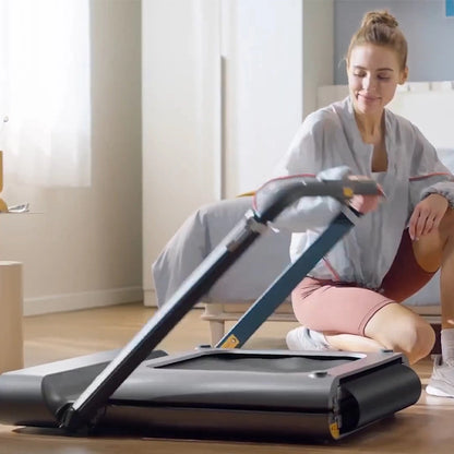 Eine Frau kniet auf dem Boden und klappt das Kingsmith WalkingPad R1H/R1 Pro 2IN1 klappbares Laufband in einem hellen, modernen Schlafzimmer zusammen.