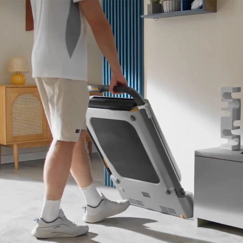Eine Person in kurzen Hosen und Turnschuhen faltet und bewegt ein Kingsmith WalkingPad R1H/R1 Pro 2IN1 klappbares Laufband in einem modernen Wohnzimmer.