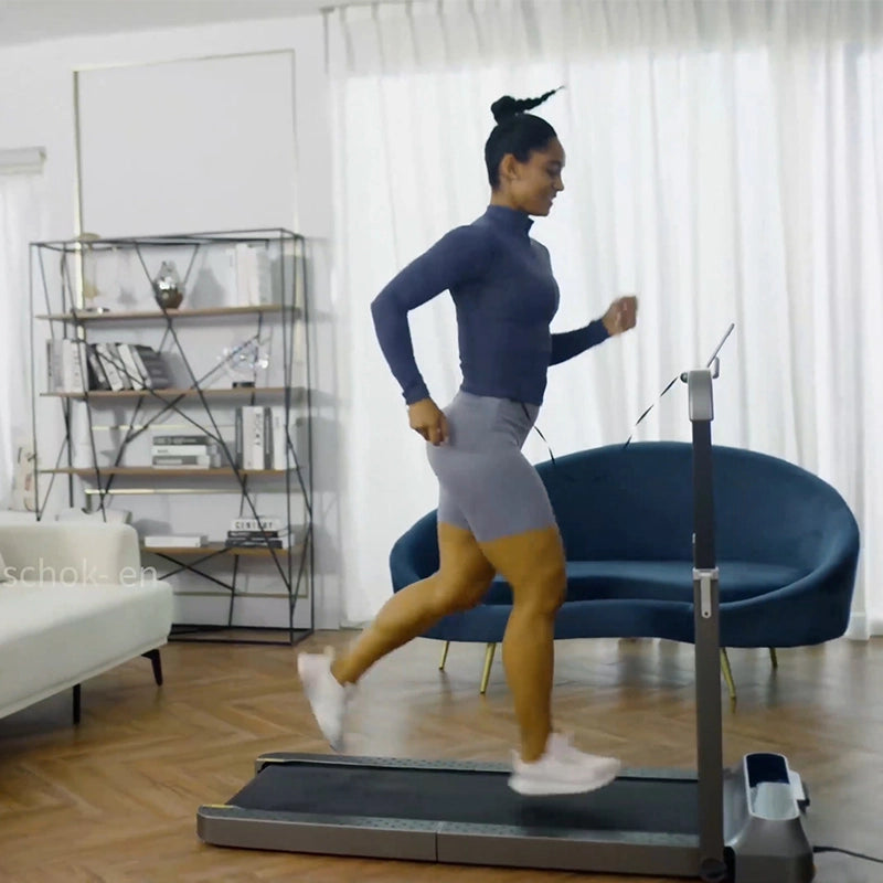 Eine Frau läuft auf einem Kingsmith WalkingPad R2/R2H Walk&Run 2IN1 faltbares Laufband in einem Wohnzimmer mit einem blauen Sofa, weißen Vorhängen und einem Bücherregal im Hintergrund.