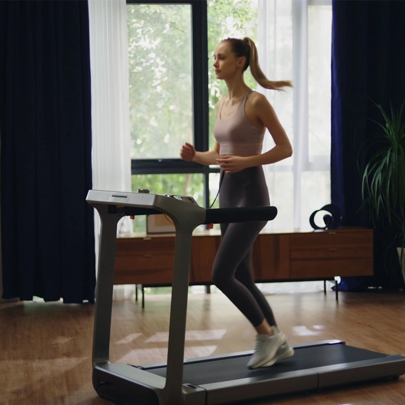 In einem hellen, modernen Wohnzimmer mit Holzfußboden und großen Fenstern läuft eine Frau in Sportkleidung auf dem Kingsmith WalkingPad X218 Klappbares Laufband und macht intensives Training zu ihrer täglichen Routine.