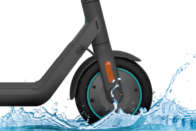 Nahaufnahme des Vorderrads eines Elektrorollers, das vor einem weißen Hintergrund durch Wasser spritzt.
