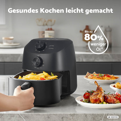 Eine Hand nimmt einen Korb mit fertig gebratenen Pommes frites aus der „aeco Cube 2.0 Airfryer 2 Liter“ auf einer Küchenarbeitsplatte, neben der Teller mit Speisen stehen, und verdeutlicht damit gesundes Kochen in einem modernen Ambiente.