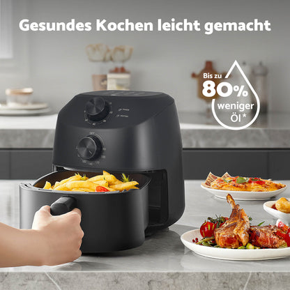 Eine Hand holt Pommes frites aus einer aeco Cube 2.0 Airfryer 2 Liter, die neben Tellern mit gebratenem Hähnchen und Gemüse auf dem Tisch steht – perfekt für jede kompakte Küche. Der deutsche Text darüber wirbt für gesünderes Kochen mit weniger Öl.