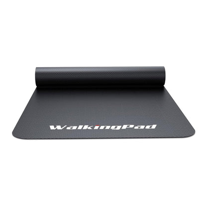 Eine schwarze, strukturierte, rutschfeste Kingsmith WalkingPad Laufband-Bodenmatte, die teilweise ausgerollt ist, trägt am unteren Rand den Aufdruck „WalkingPad“ in weißer Schrift.