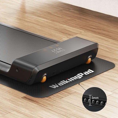 Eine Nahaufnahme eines schwarzen Kingsmith WalkingPad-Laufbands auf der rutschfesten Laufband-Bodenmatte, wobei ein eingefügter Kreis die 3 mm starke Matte hervorhebt. Das Laufband steht auf einem Holzboden.