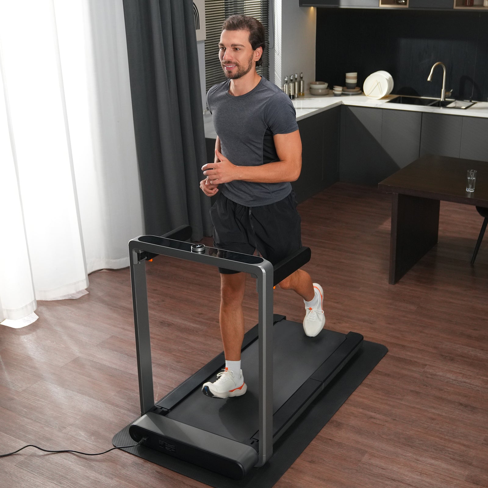 Ein Mann in Sportkleidung benutzt das Kingsmith WalkingPad X214 Klappbares Laufband in einem modernen Wohnzimmer mit Holzböden und einer im Hintergrund sichtbaren Küche.