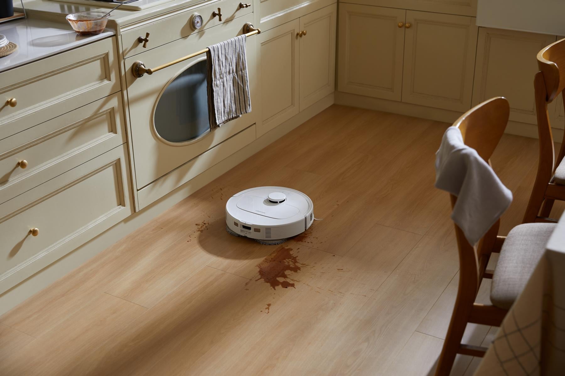 Der Roborock Qrevo 598 White Saugroboter gleitet über einen Küchenboden und verteilt eine braune Flüssigkeit.
