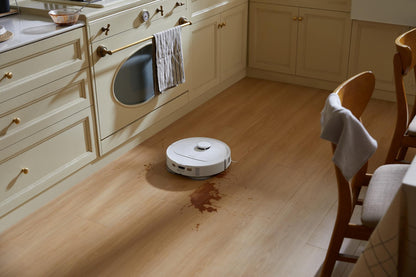Der Roborock Qrevo 598 White Saugroboter gleitet über einen Küchenboden und verteilt eine braune Flüssigkeit.