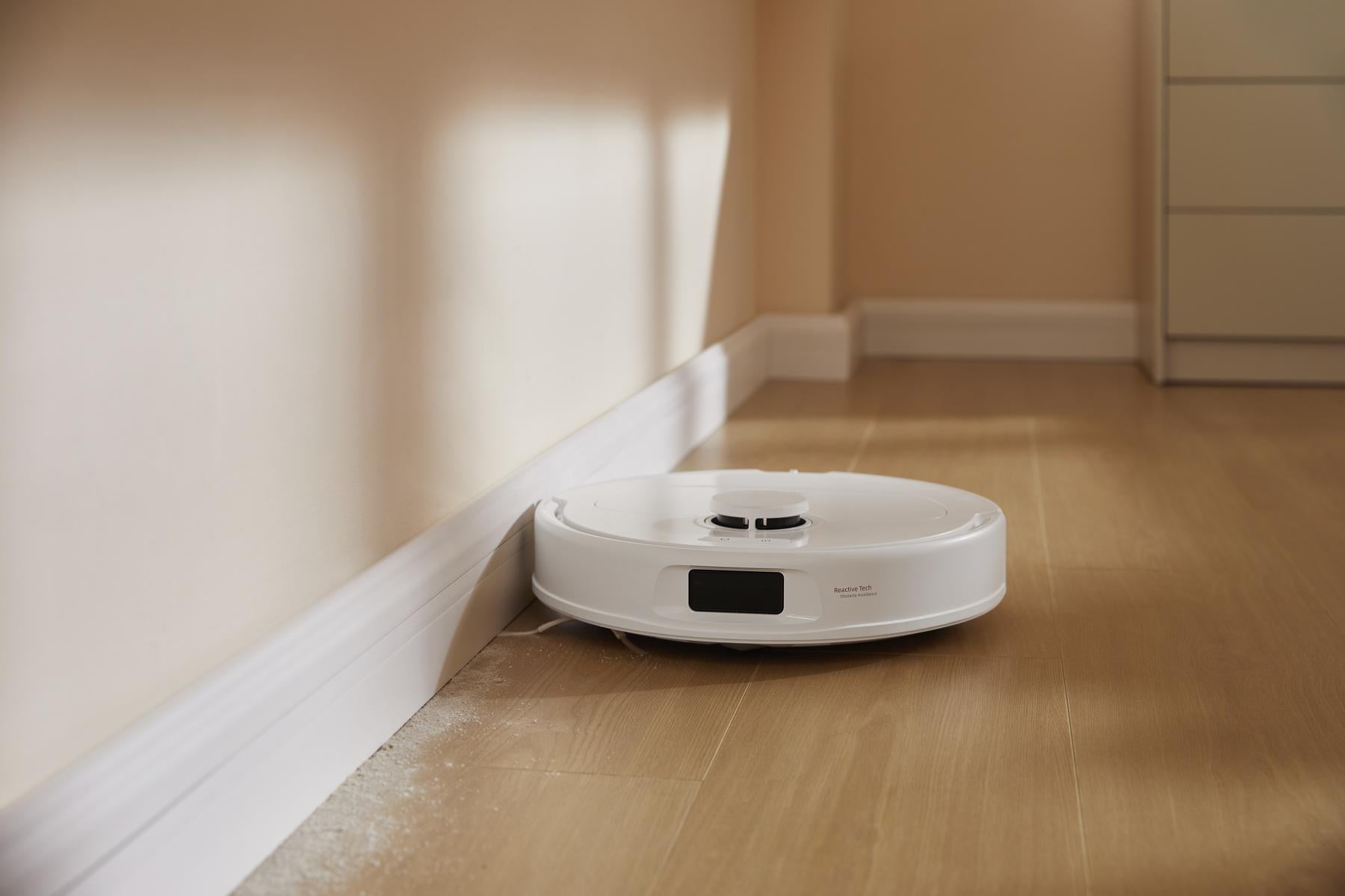 Der Roborock Qrevo 598 White, ausgestattet mit HyperForce-Saugkraft, gleitet über einen hellen Holzboden und reinigt effizient Staub entlang einer beigen Wand und Fußleiste.